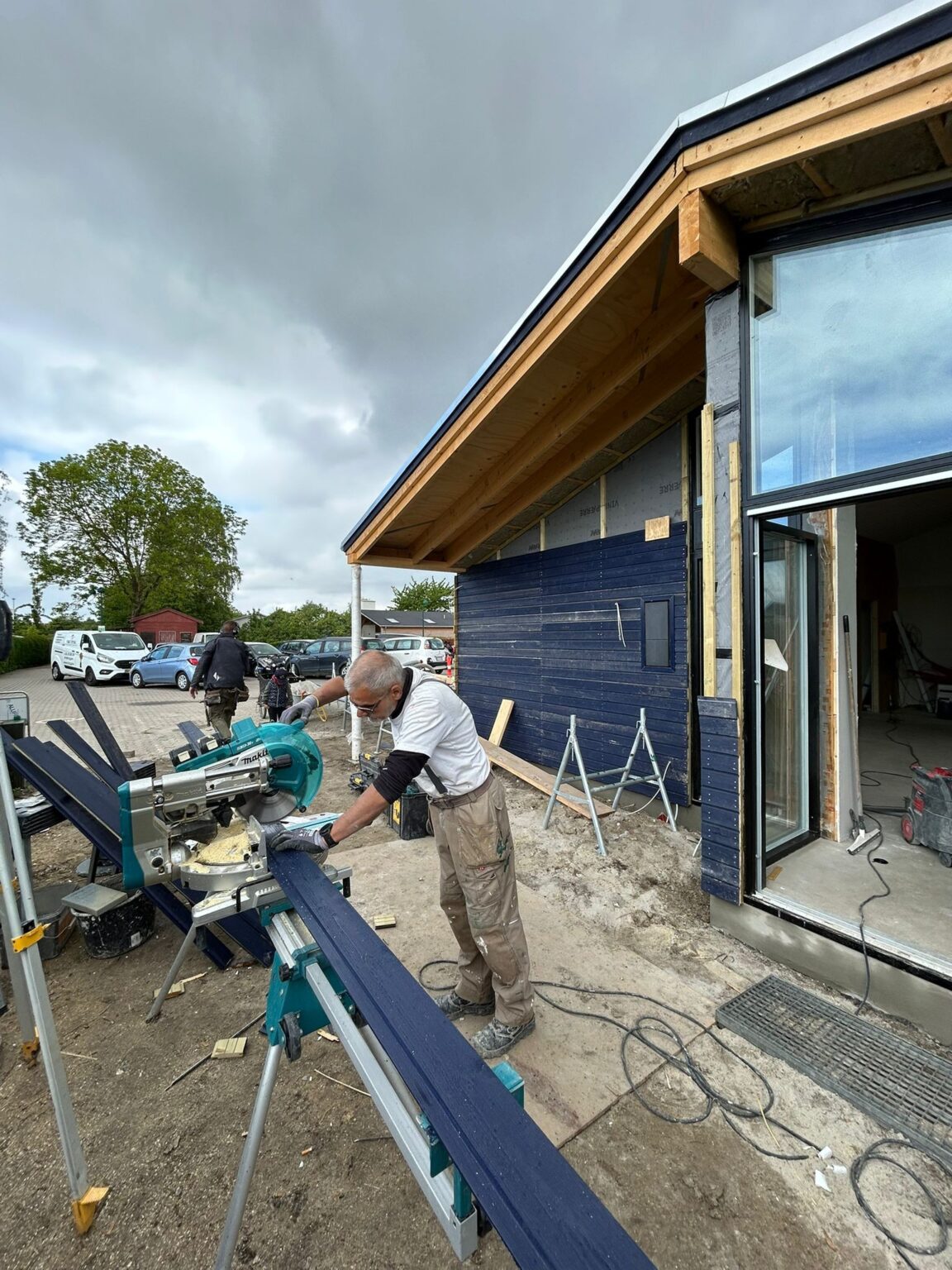 Håndværker saver træ foran nyt husbyggeri